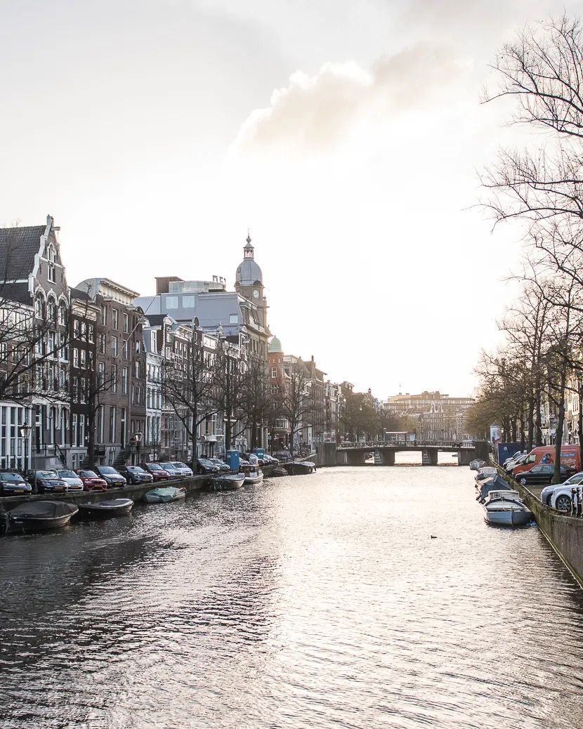 Warm golden hour light over an Amsterdam canal with historic buildings and boats along the water.
