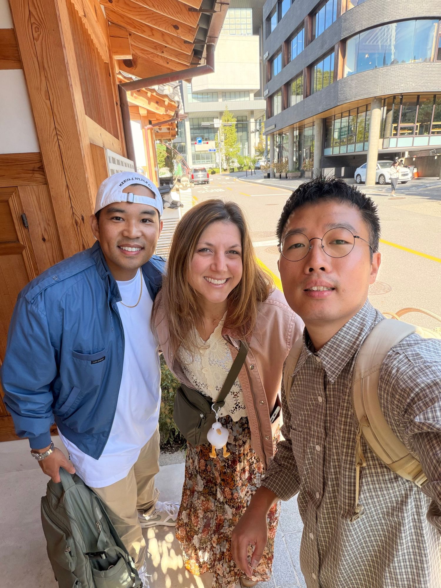 A group of friends posing together outdoors near modern buildings in casual attire on a sunny day.