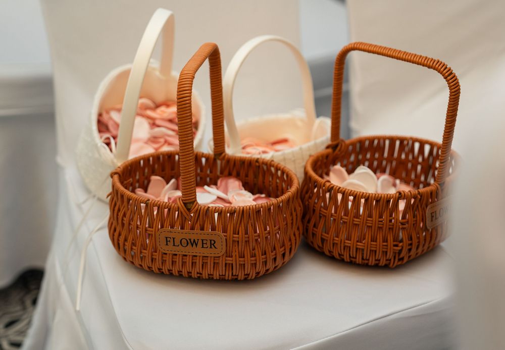 Two brown woven wicker flower girl baskets with white satin lining sit on a white surface.