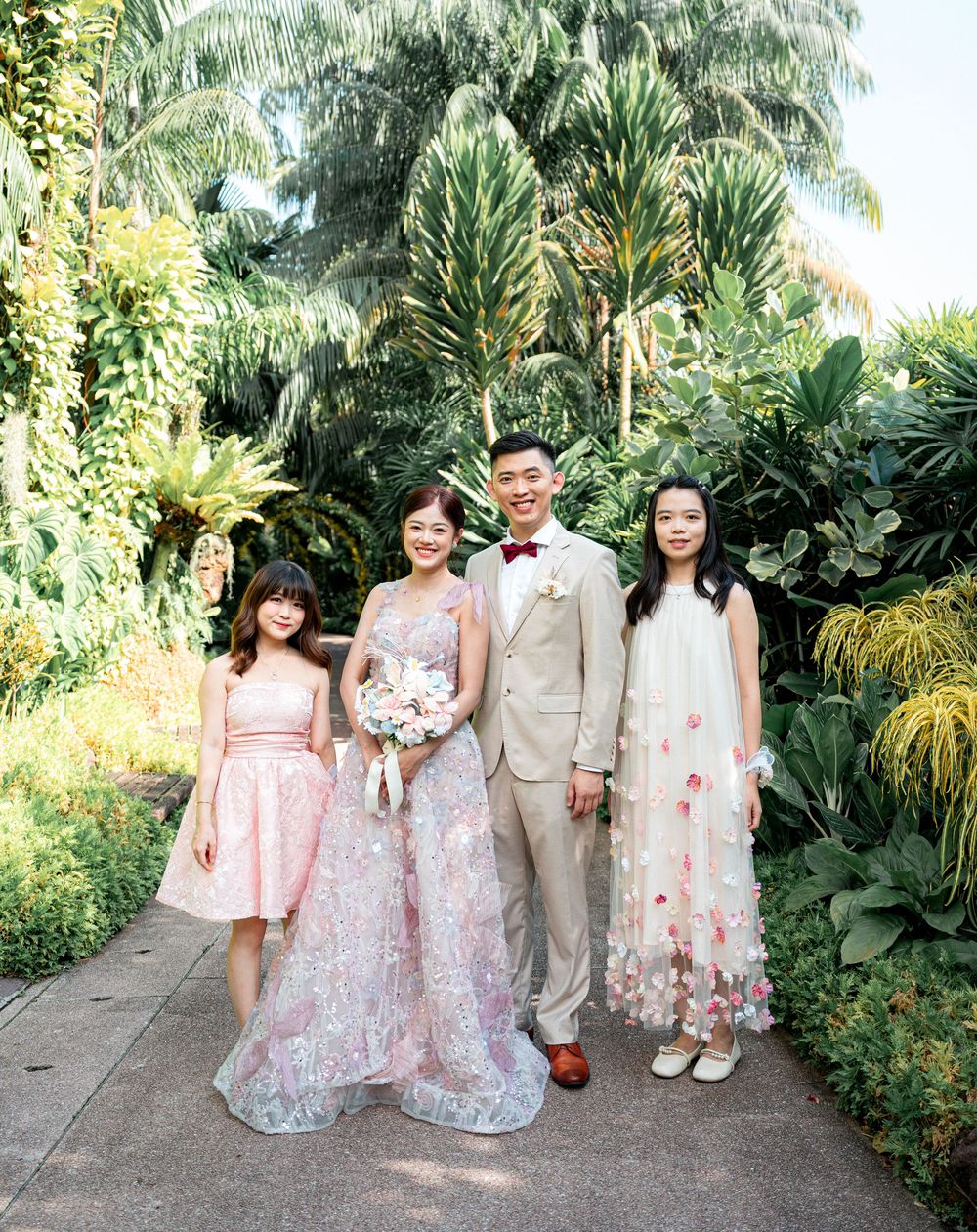 A wedding party poses on a garden path surrounded by lush tropical plants and palm trees.