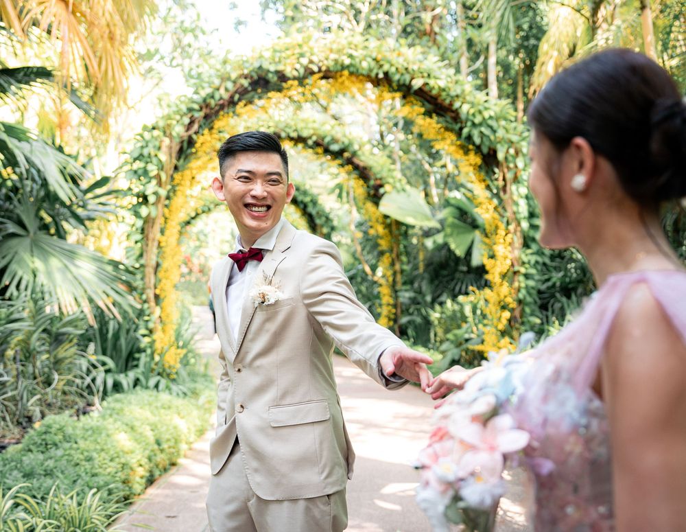 A wedding couple shares joyful moments under a yellow floral arch in a lush garden setting.