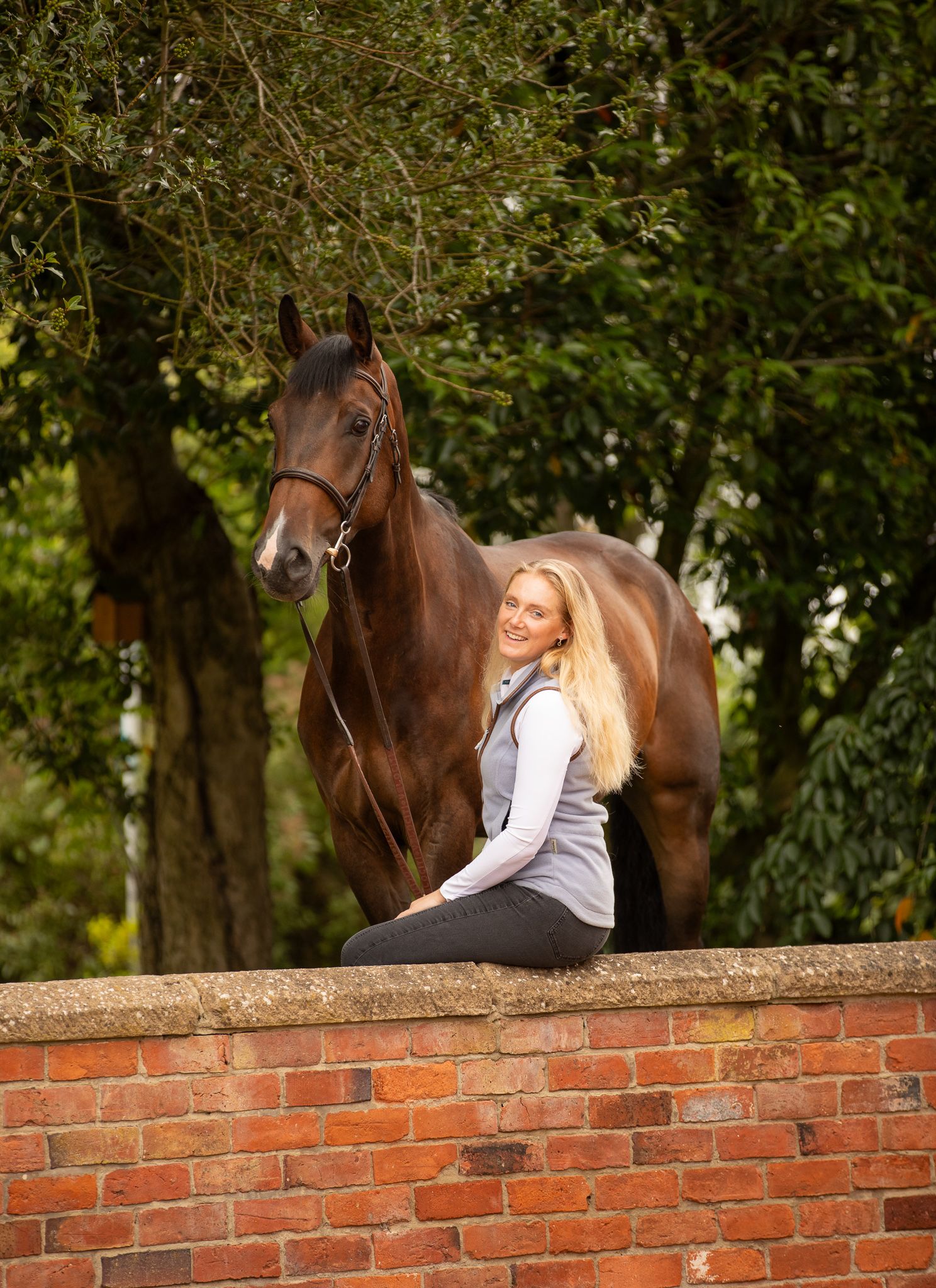 Young girl in denim overalls embraces a palomino horse in a sun-dappled forest setting.