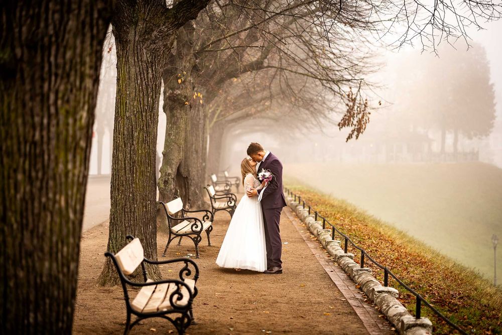 A romantic moment captured on a misty path lined with benches and trees in autumn.