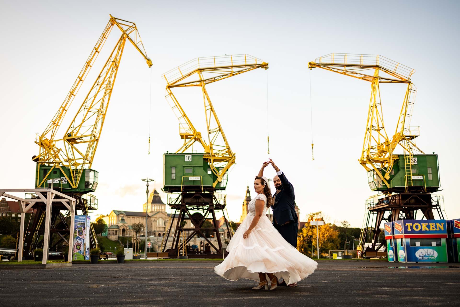 A romantic wedding photoshoot silhouette against industrial cranes at sunset creates a dramatic urban backdrop.