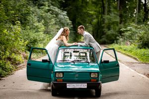 A turquoise vintage car parked in a lush forest setting with its doors open for a romantic photoshoot.
