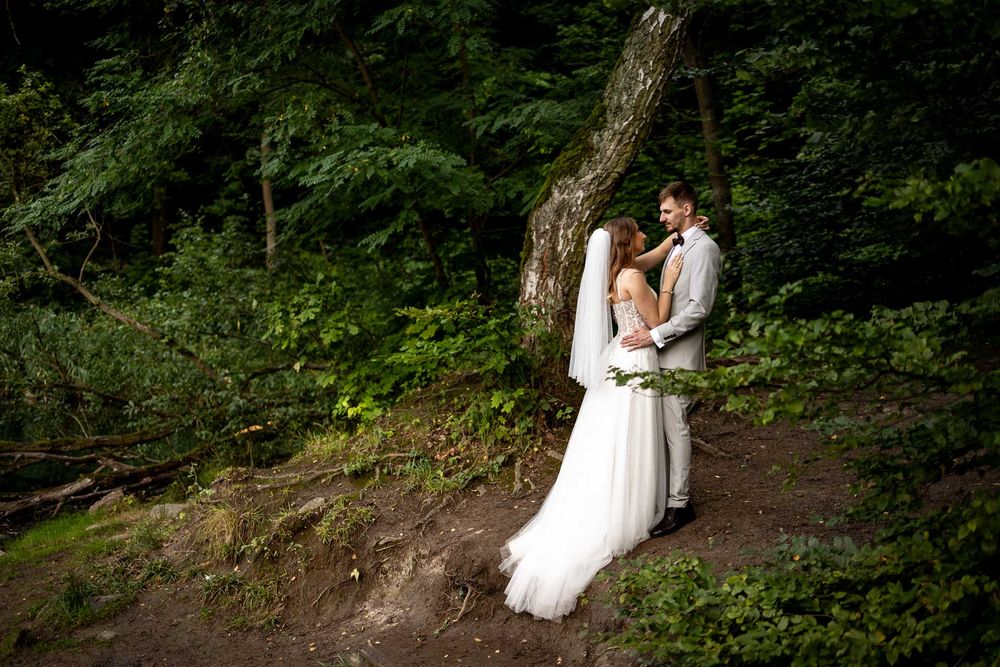 A couple in wedding attire walks through a lush forest setting during their outdoor wedding photoshoot.