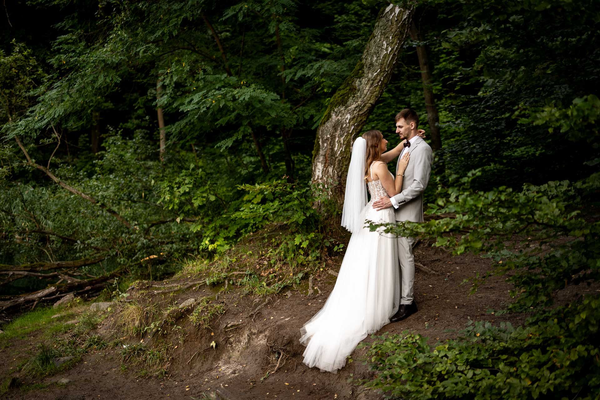 A couple in wedding attire walks through a lush forest setting during their outdoor wedding photoshoot.