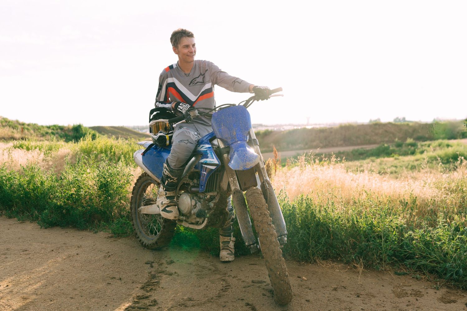 Riders taking a break with their dirt bikes on a grassy hillside during sunset.