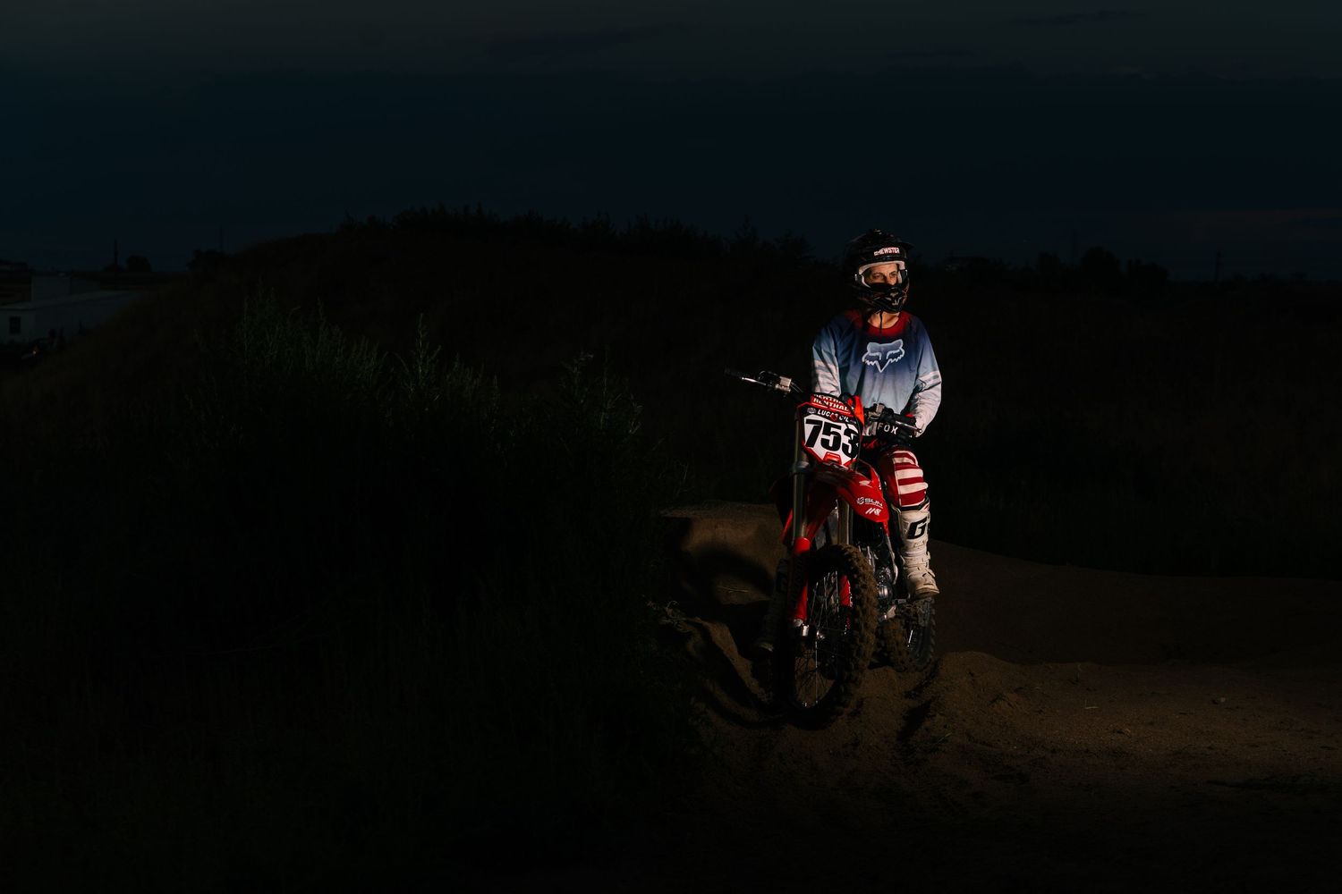 Dirt bike riders racing along a dark trail at dusk with dramatic lighting.