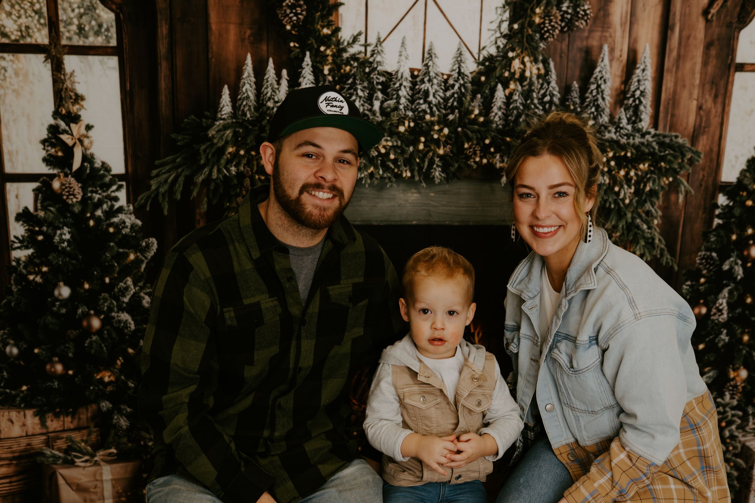 Cozy indoor family portrait session with rustic wooden and greenery backdrop.