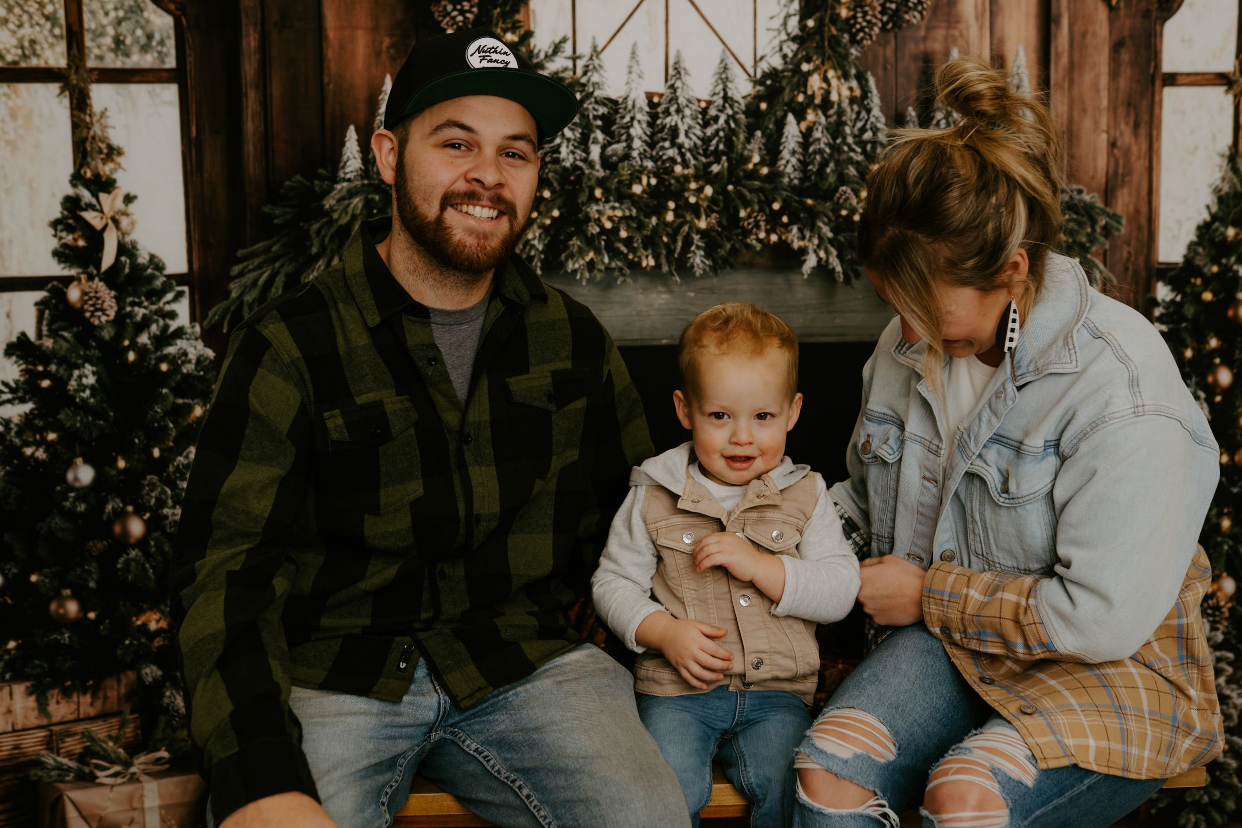 Family poses together in casual attire against rustic holiday-themed backdrop.