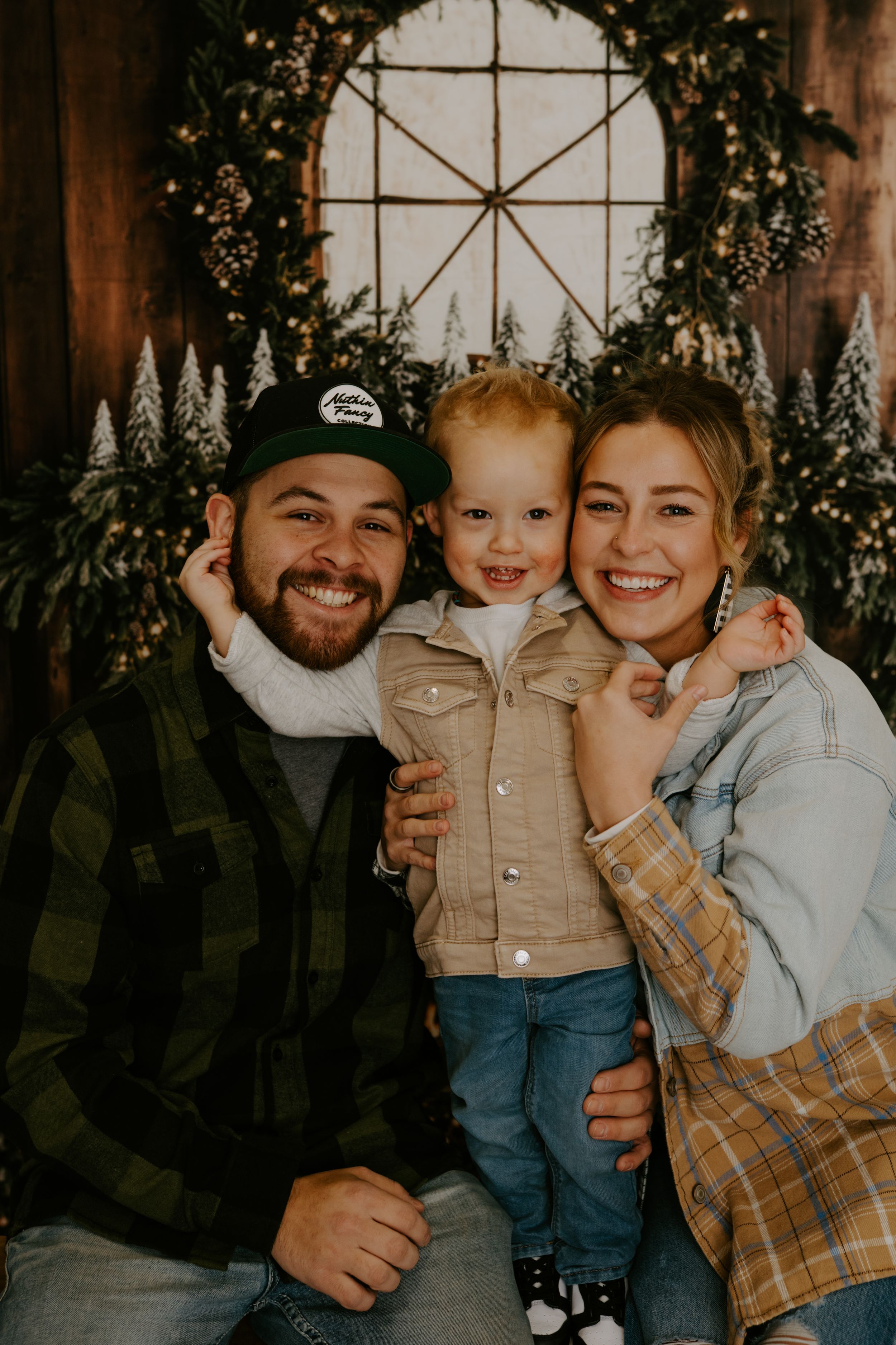 Warm family portrait with holiday decorations and wooden backdrop.