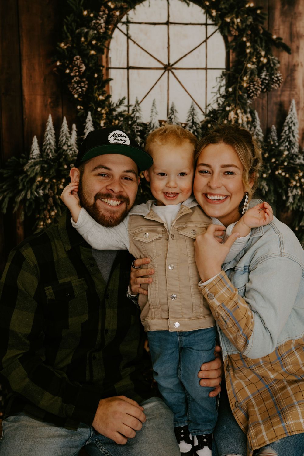 Warm family portrait with holiday decorations and wooden backdrop.