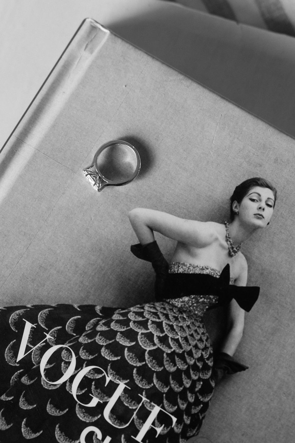 A vintage black and white fashion photograph featuring a Vogue magazine cover and an elegant evening gown.