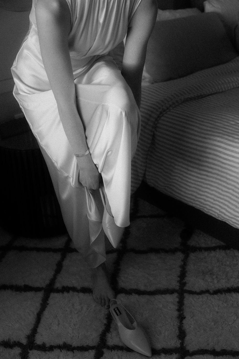 Monochrome image showing the lower portion of flowing white dresses against a patterned carpet.