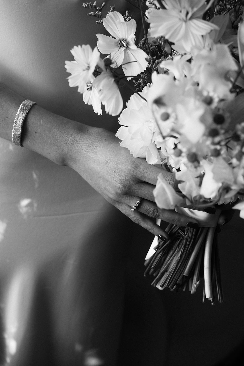 Close-up black and white photograph of hands holding a delicate white floral bouquet.