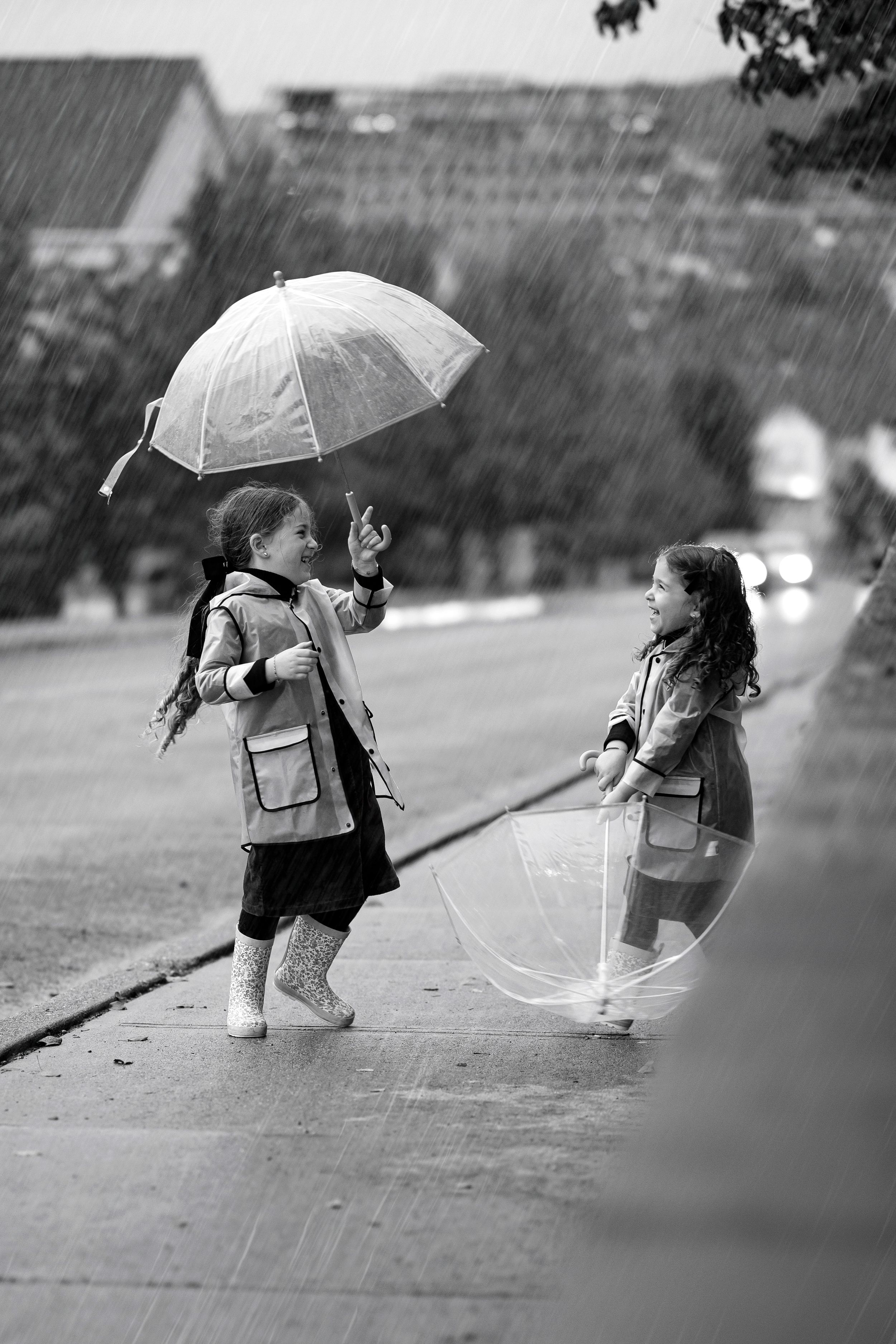 Children walking together with clear umbrellas on a rainy day captured in black and white.