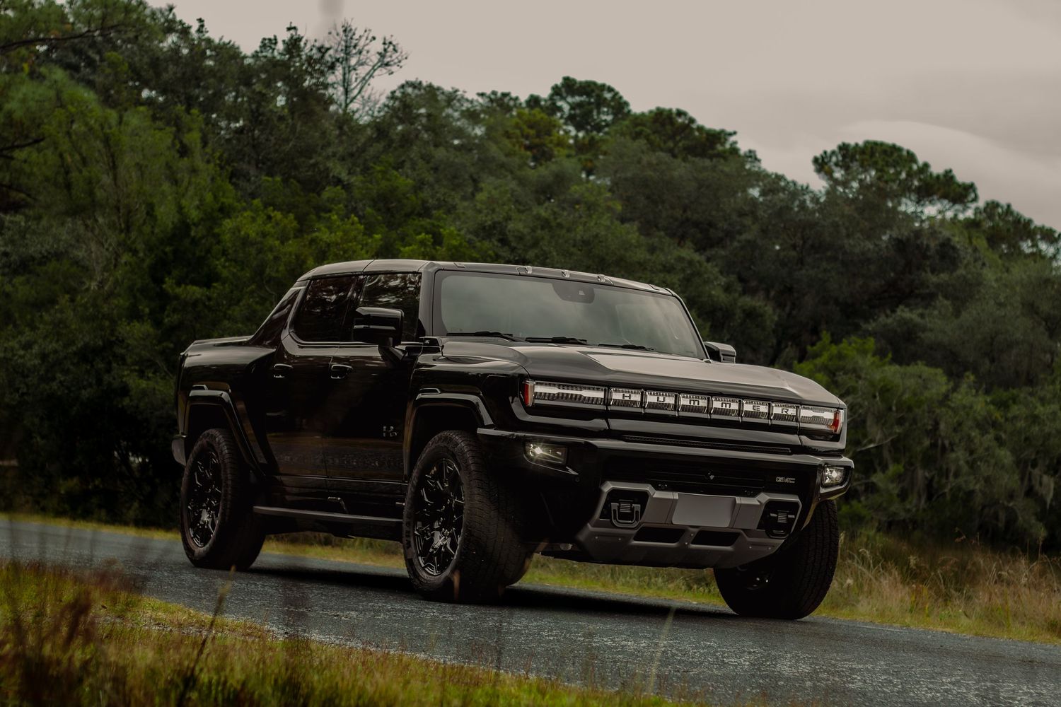 A black Ford pickup truck driving on a rural road surrounded by green trees and vegetation.