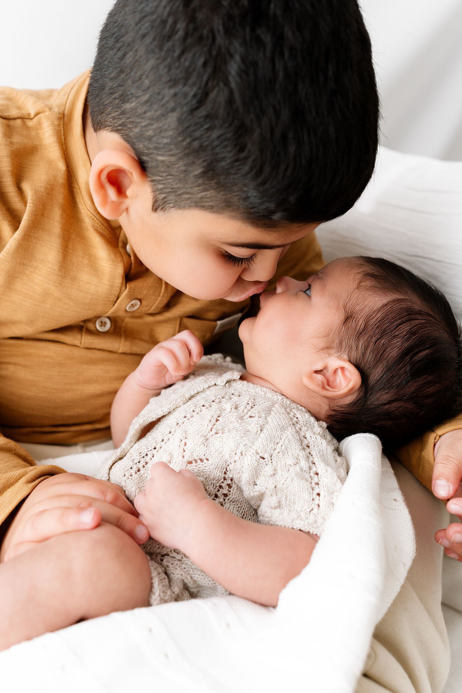 A tender moment between a bearded parent in white and a baby in a lace dress against a light background.