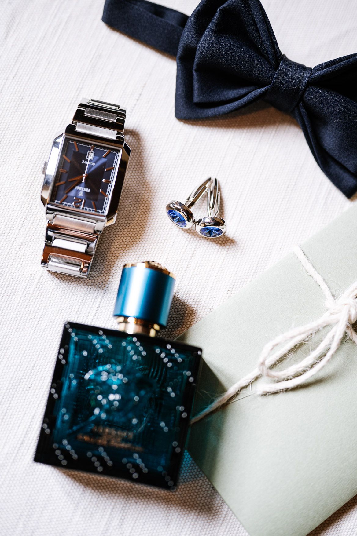 Black bow tie and silver cufflinks with turquoise accents arranged on white textured surface for formal attire styling.