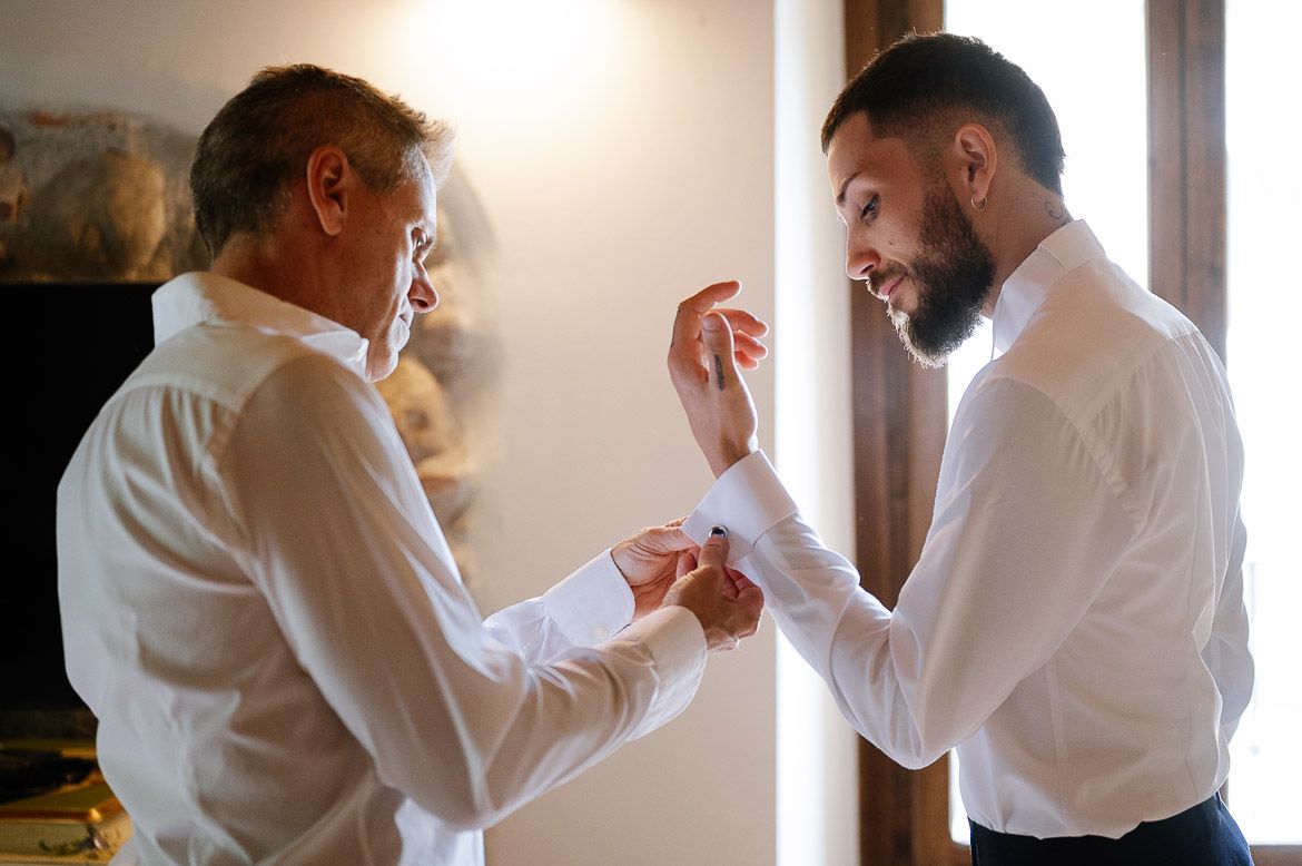 A person in a white shirt adjusts their collar and cuffs while getting dressed in a formal outfit.