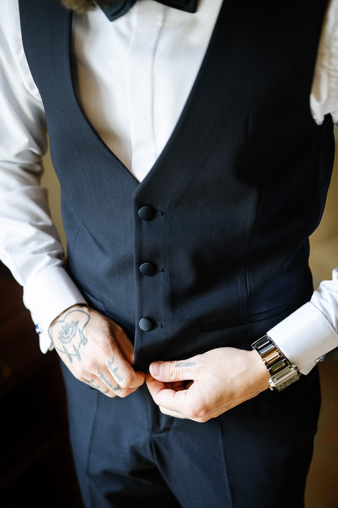 Close-up shot of a formal black vest and white dress shirt being buttoned for a special occasion.