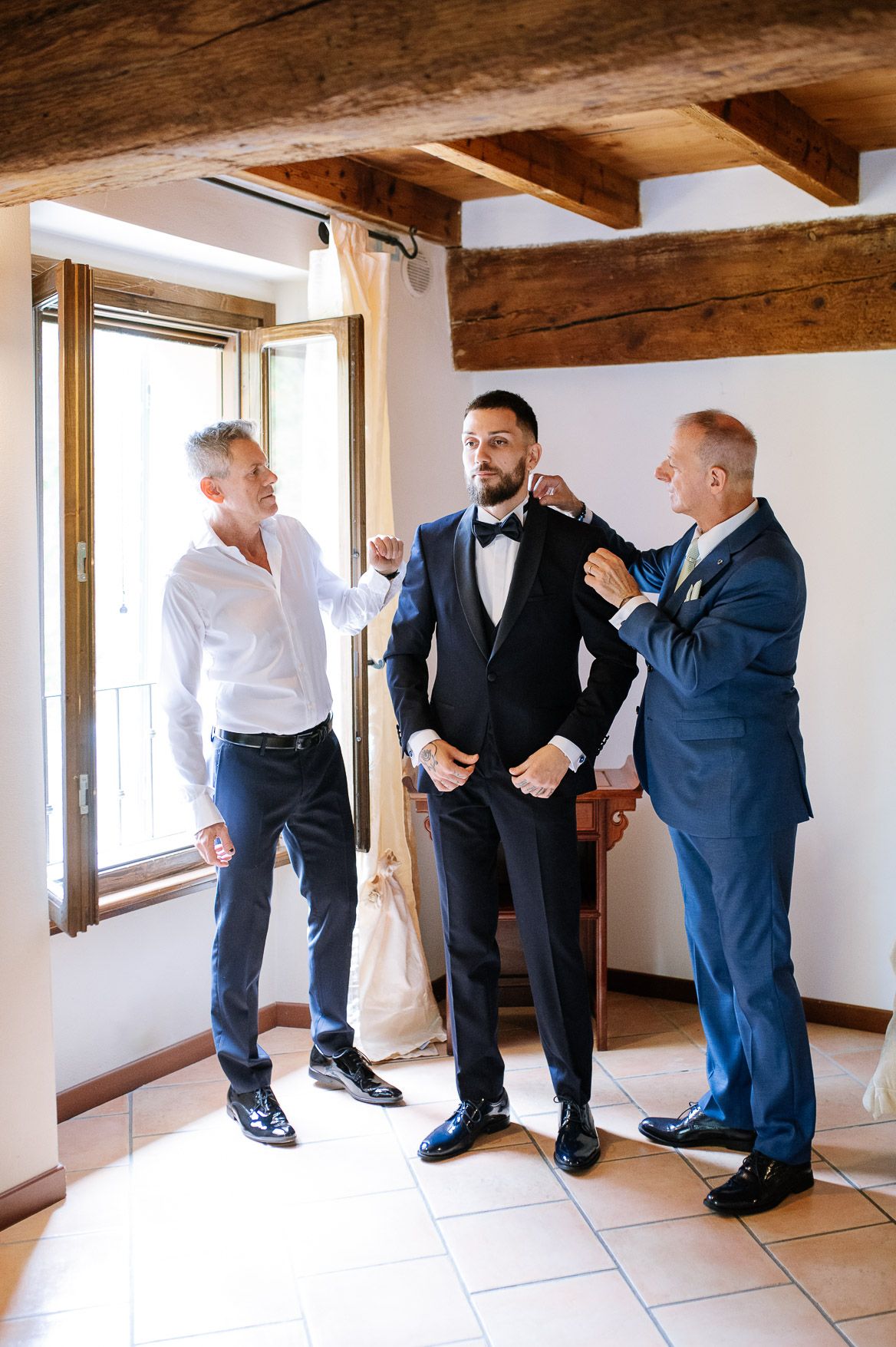Groomsmen getting ready in a rustic room with exposed wooden beams and white walls.
