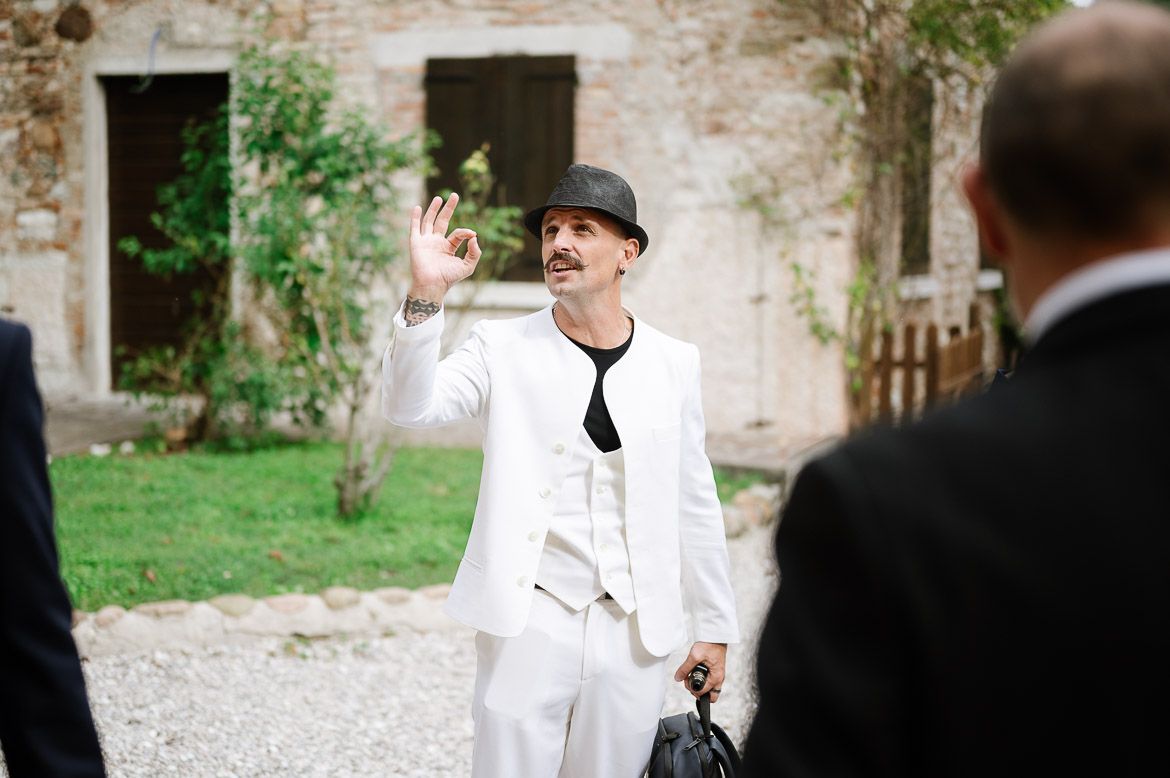 A formal outdoor wedding scene with guests in black and white attire near a stone building.