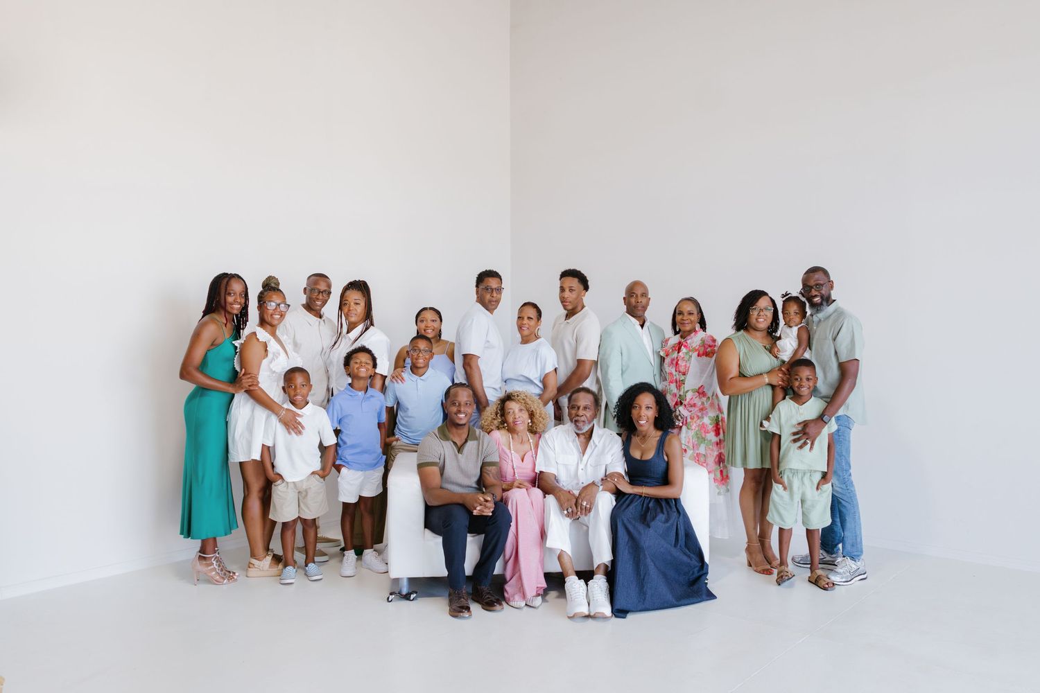 A large extended family poses together smiling on a sunny green lawn near tall pine trees.