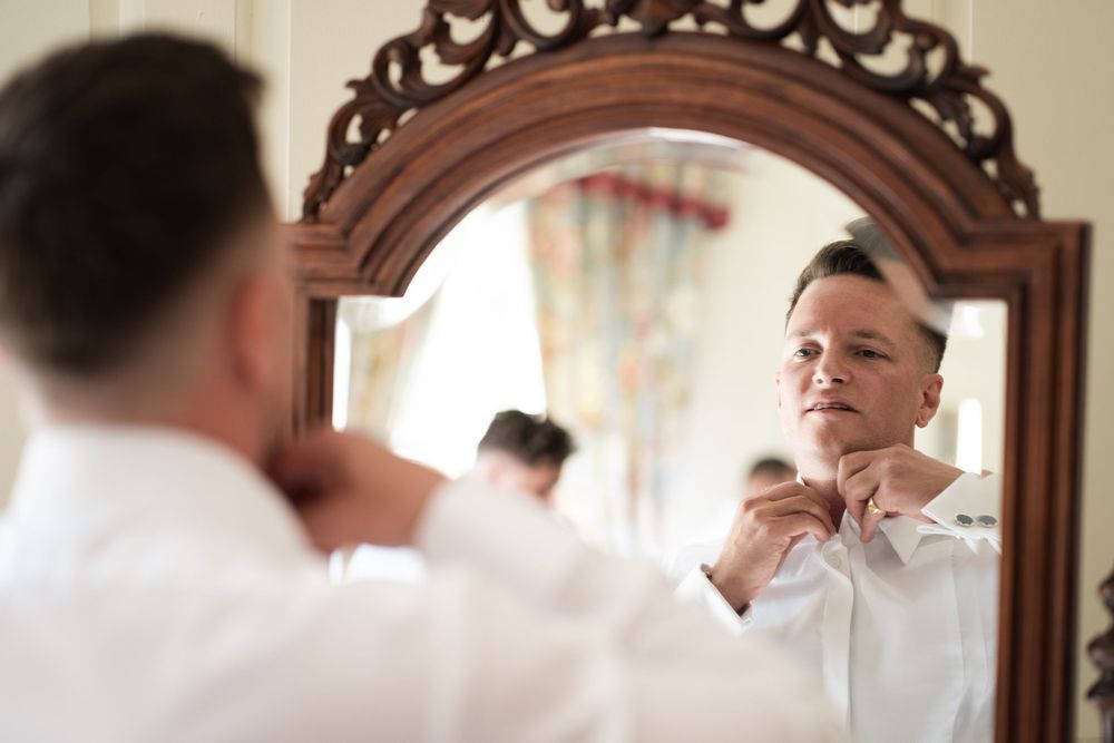 A person adjusts their tie while looking in an ornate wooden framed mirror.