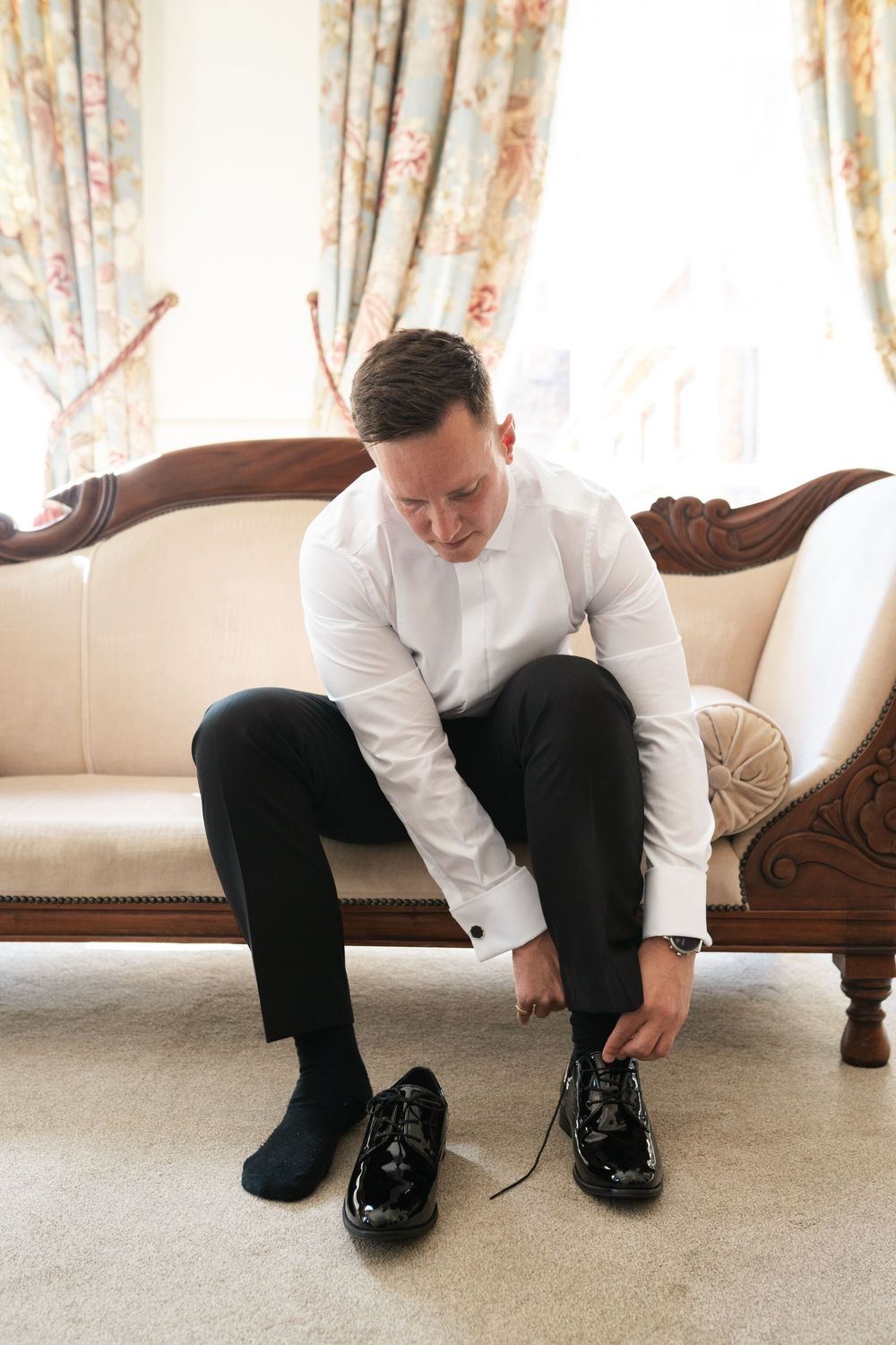 A series of four photos showing someone in formal attire tying dress shoes while sitting on a cream-colored sofa.