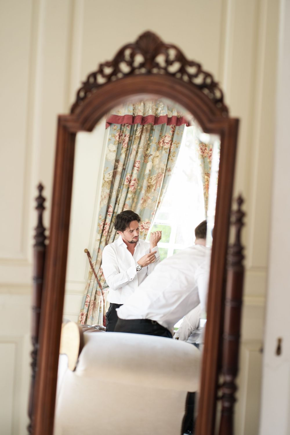 A series of three mirror reflections show a person in white clothing lounging on an elegant wooden bed frame.