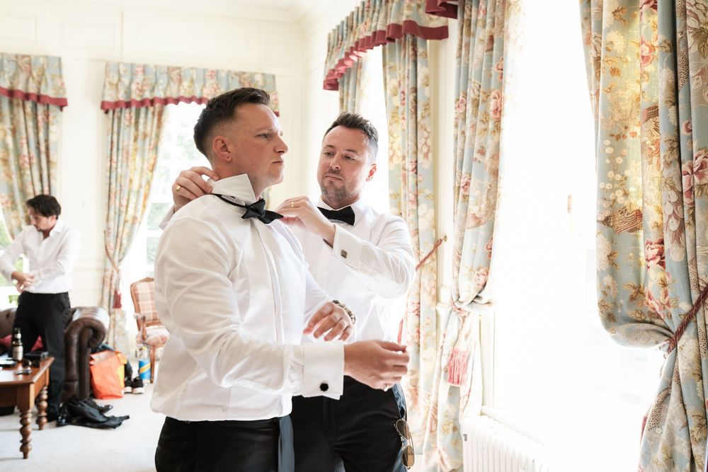 Two people in white shirts dance together in an elegant room with floral curtains and soft lighting.