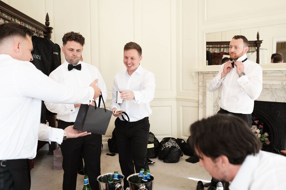 Groomsmen help each other get ready by adjusting bow ties and suits before a formal wedding ceremony.