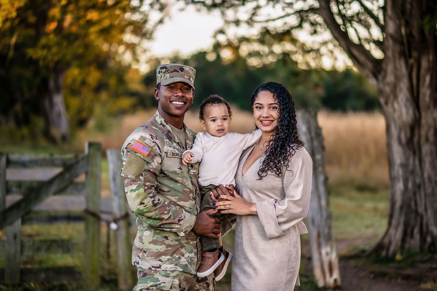 A military service member in camouflage uniform shares tender moments with family members outdoors during sunset.