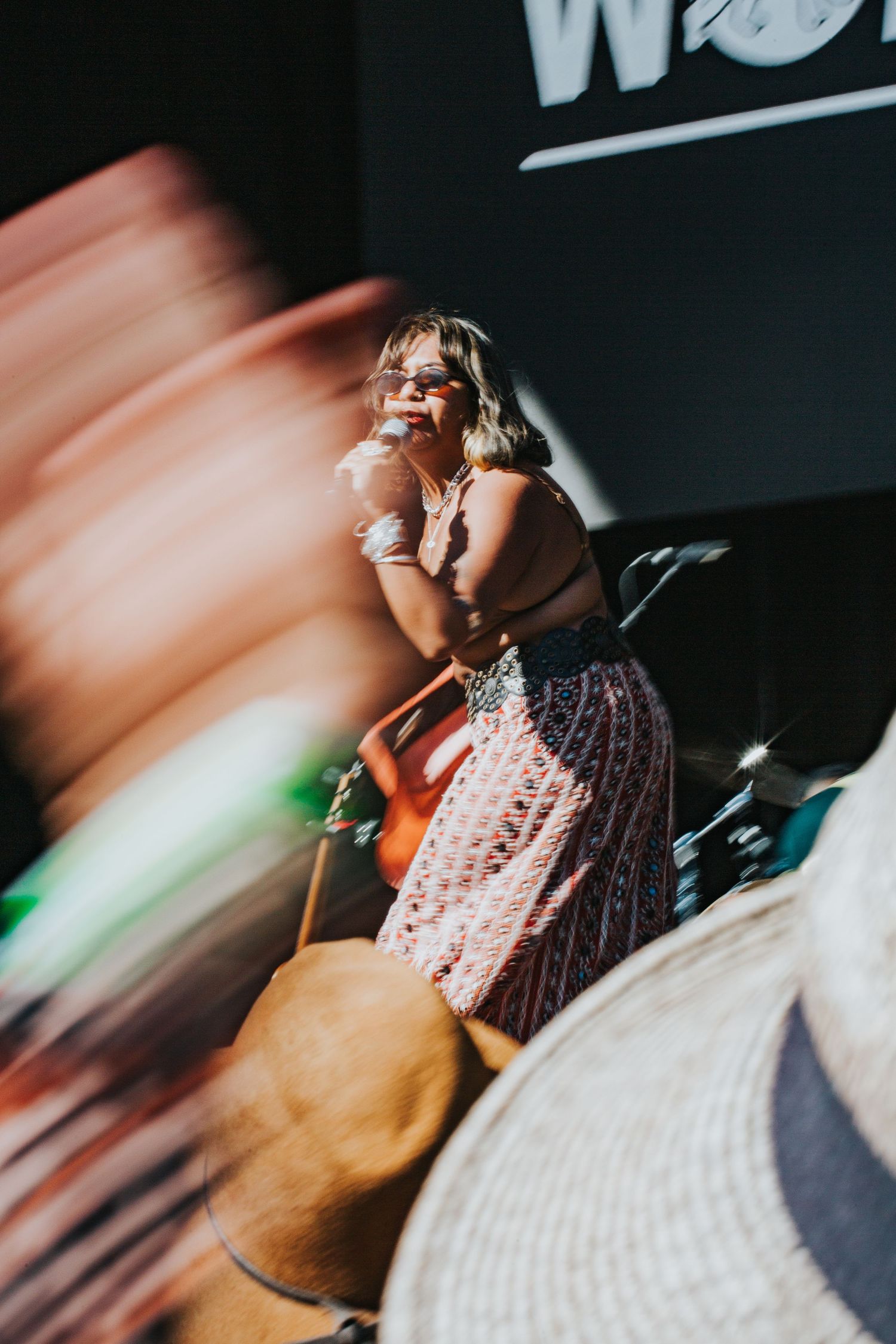 Female singer performing on stage in a floral skirt with motion blur in the foreground.