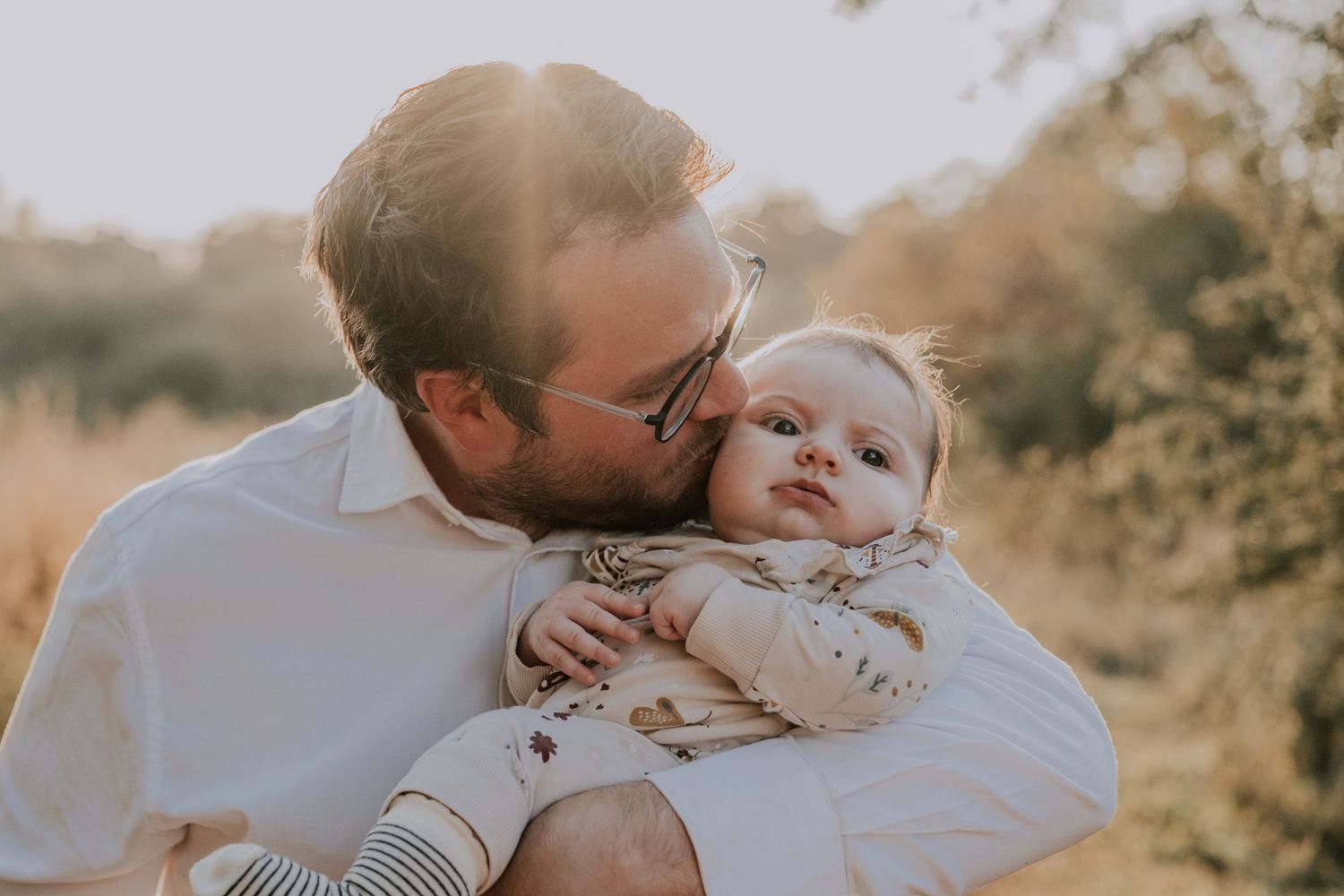 A tender moment between parent and baby outdoors during golden hour with warm sunlight in the background.
