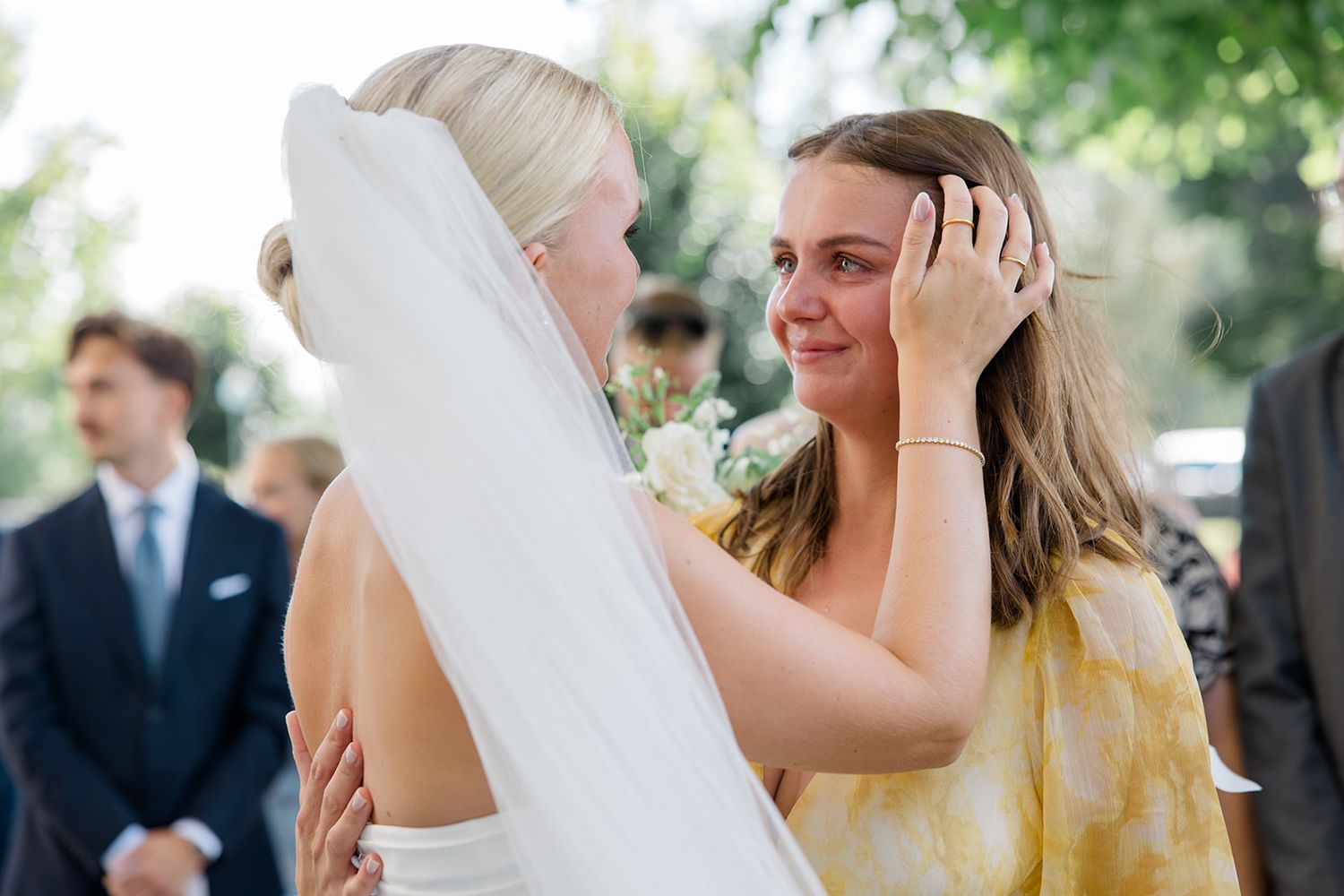 Bridesmaids in yellow dresses embrace during an emotional outdoor wedding ceremony.