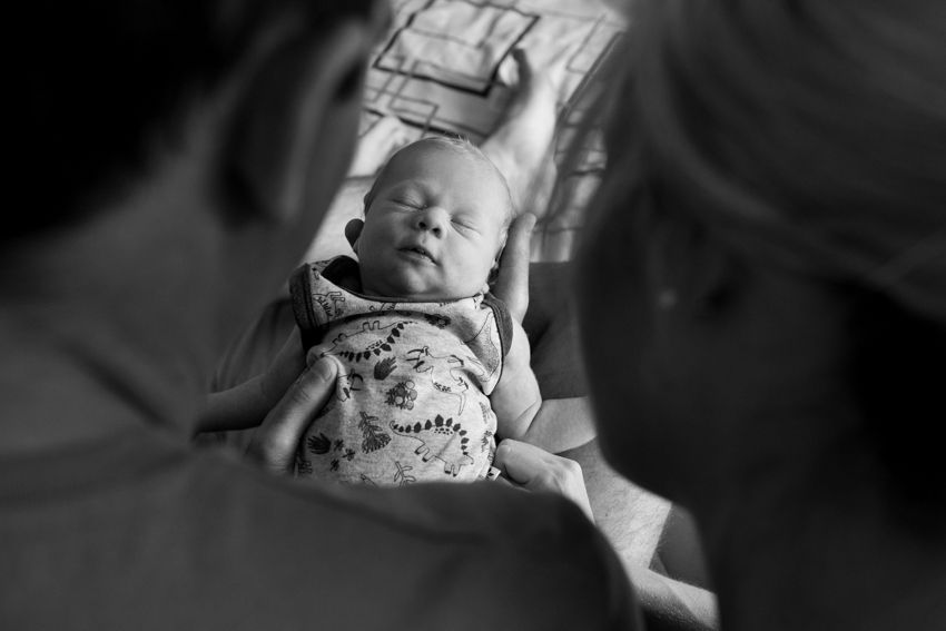 Photo of a newborn taken over the shoulder of new mum and dad. Photo in Black and white - Kelly Chapman Photographer Perth