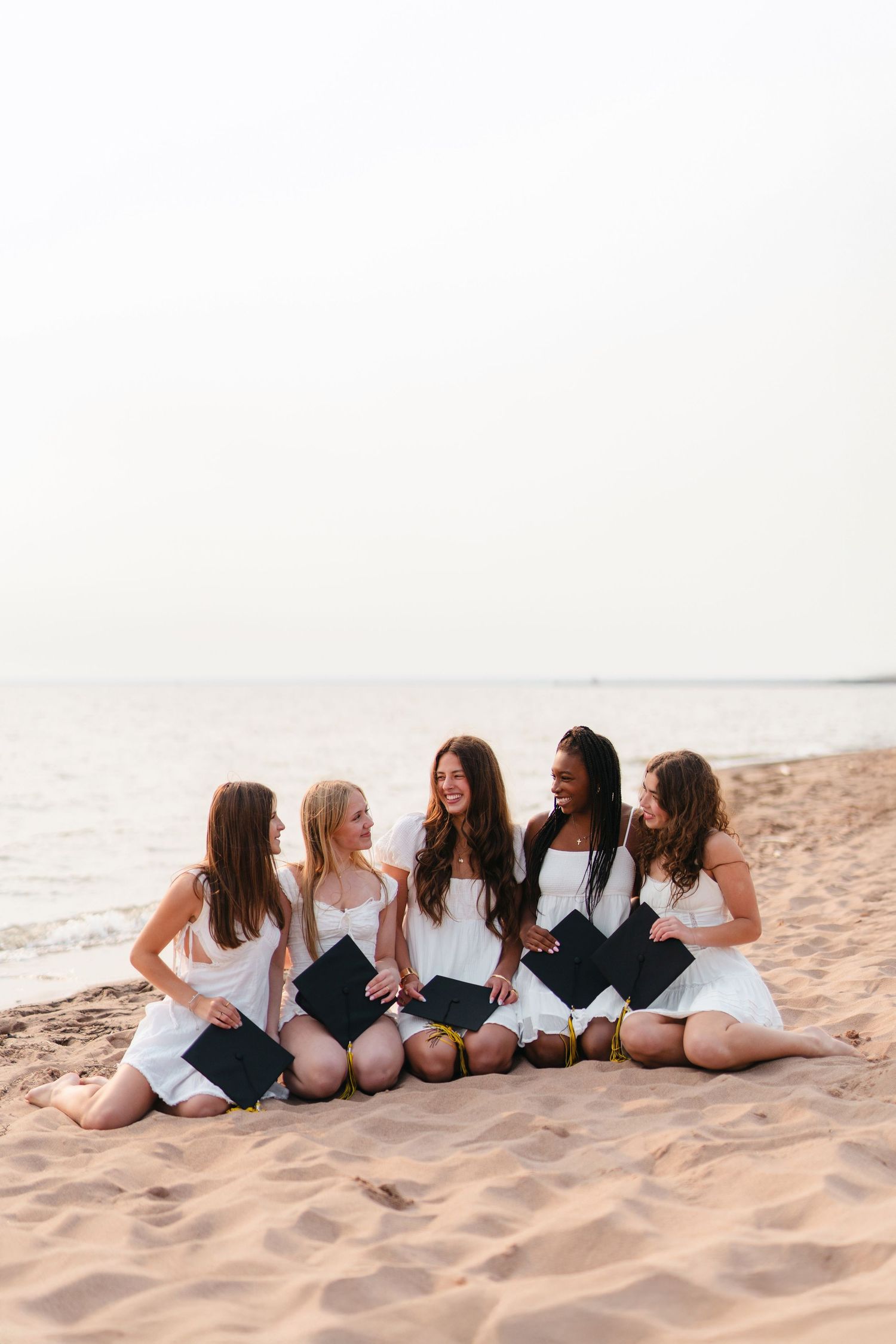 A group of friends in black and white swimsuits sitting together on a sandy beach at sunset.