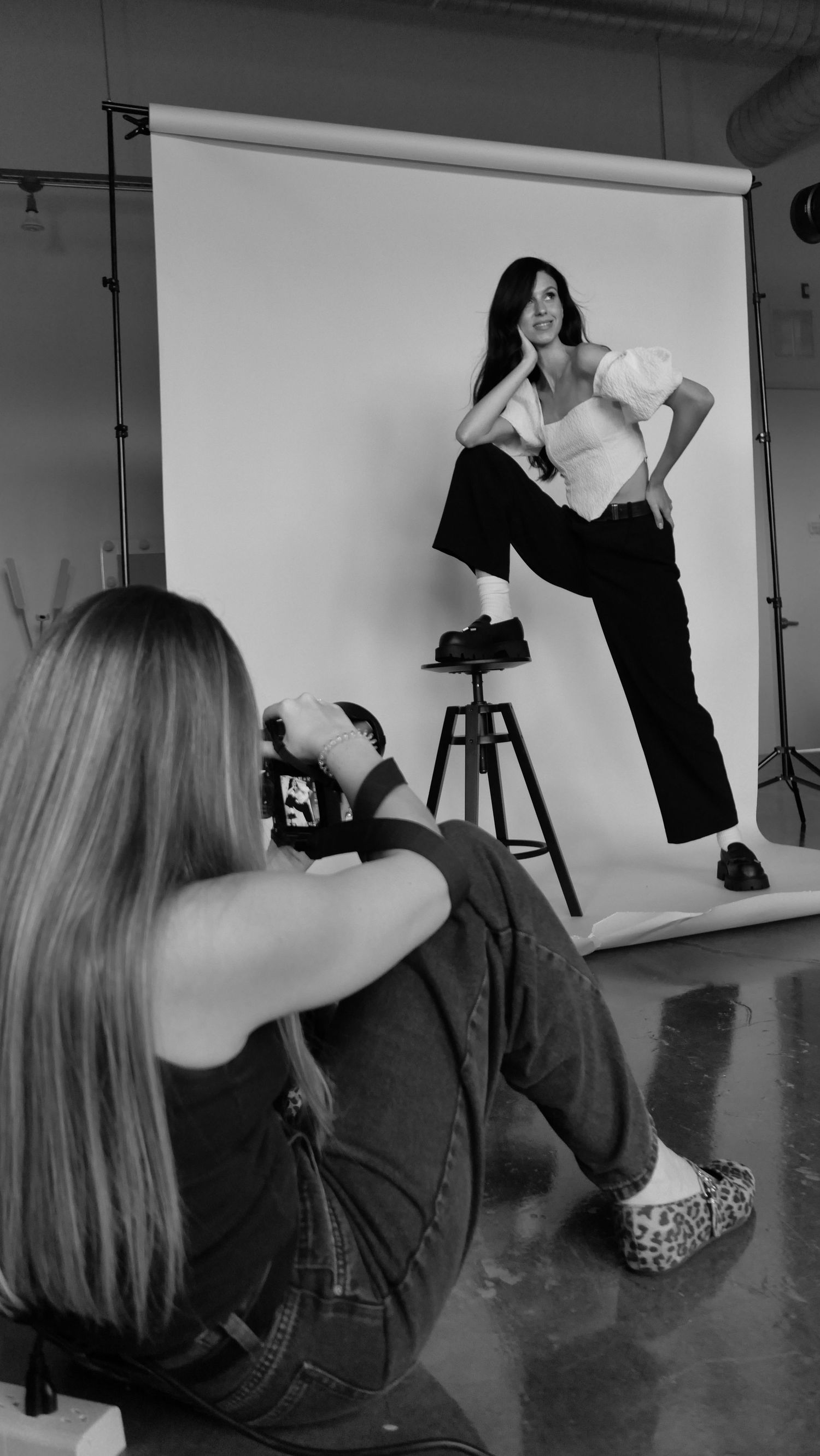 A series of black and white fashion photography behind-the-scenes shots showing a model posing on a stool in a studio setting.