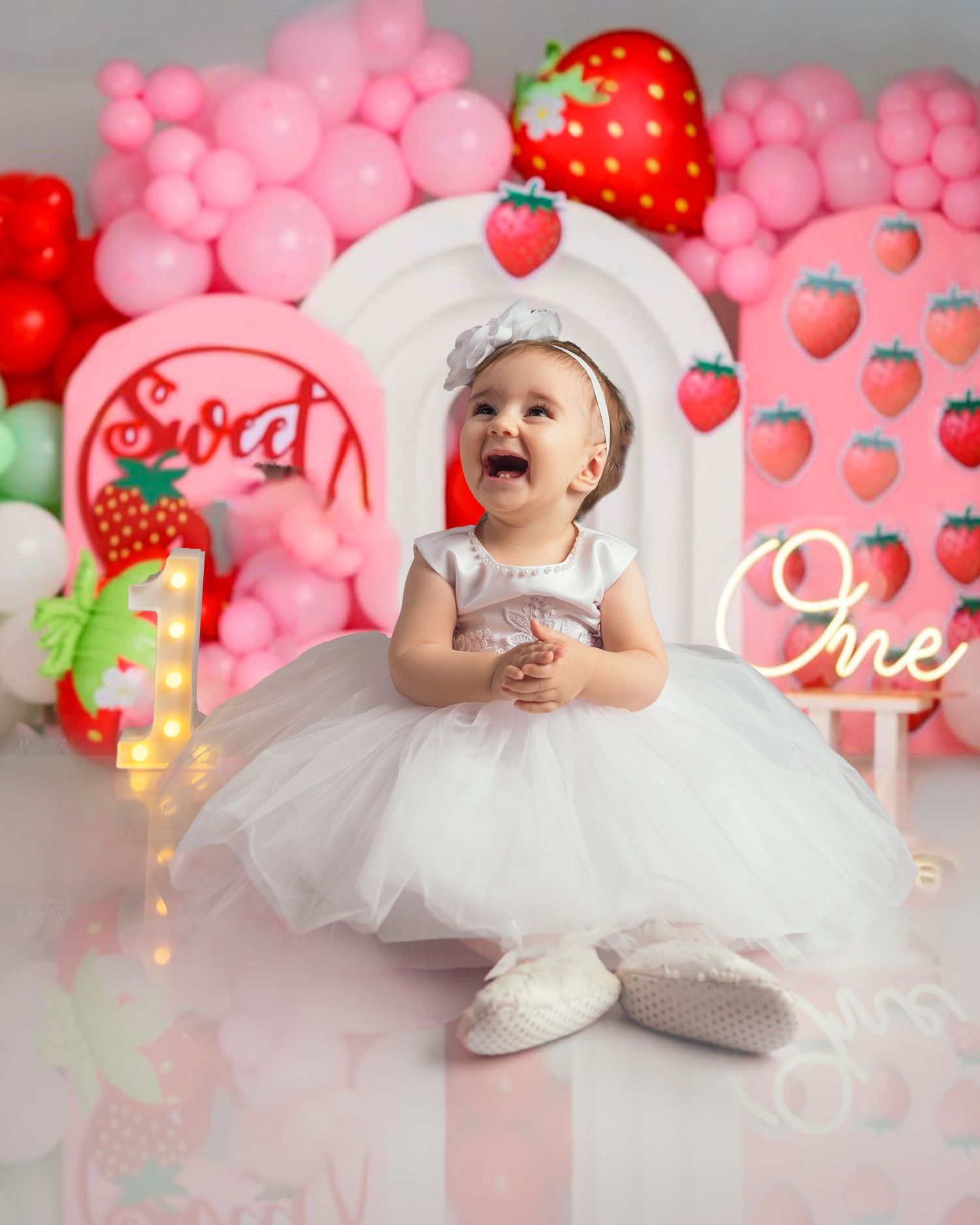 Happy baby girl in white tutu dress at strawberry themed first birthday party.