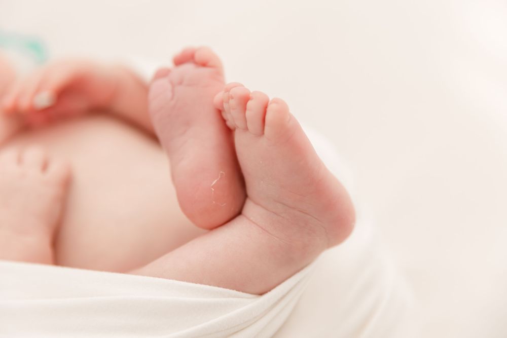 Tiny newborn baby feet and toes against a soft white background.