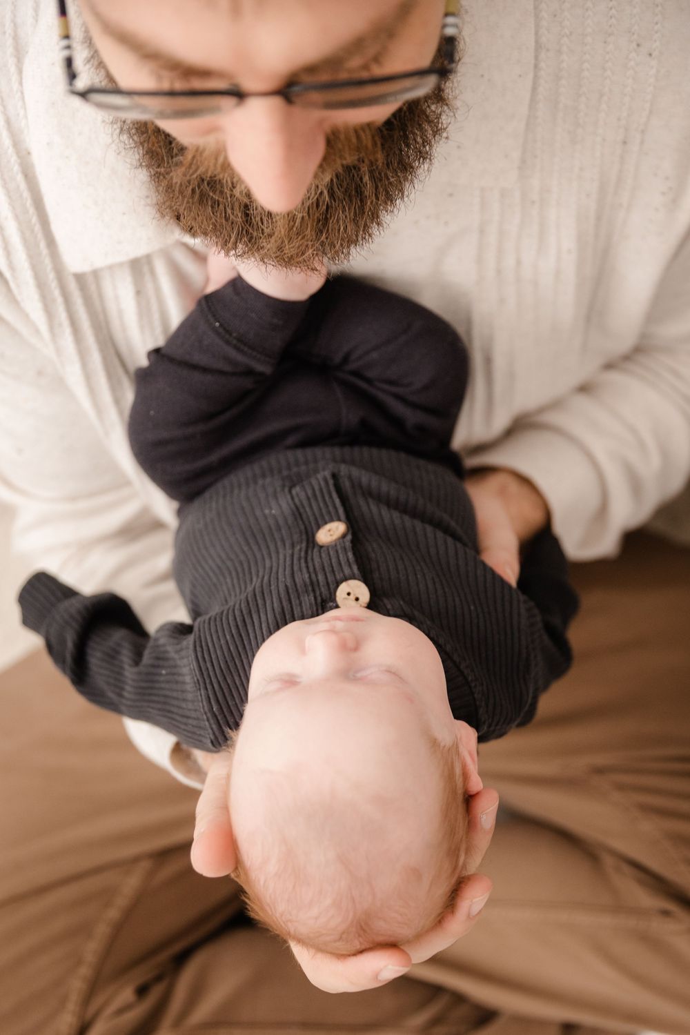 A series of photos showing a newborn baby being gently cradled in black clothing against a neutral background.