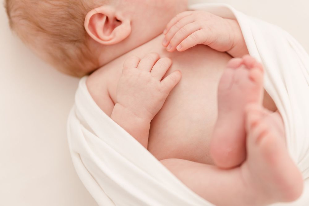 Peaceful sleeping newborn wrapped in soft white blanket against light background.