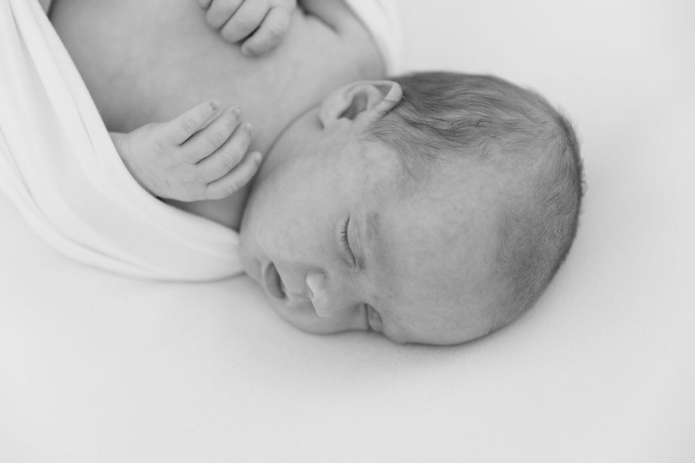 Black and white portrait of a sleeping infant resting peacefully on a soft white surface.