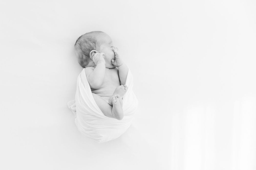 Artistic high-key newborn portrait showcasing soft curves and shadows.