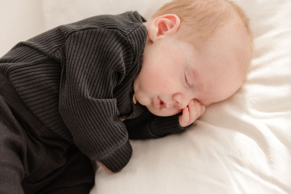 Close-up shots of a sleeping baby wearing a dark ribbed outfit on white bedding.