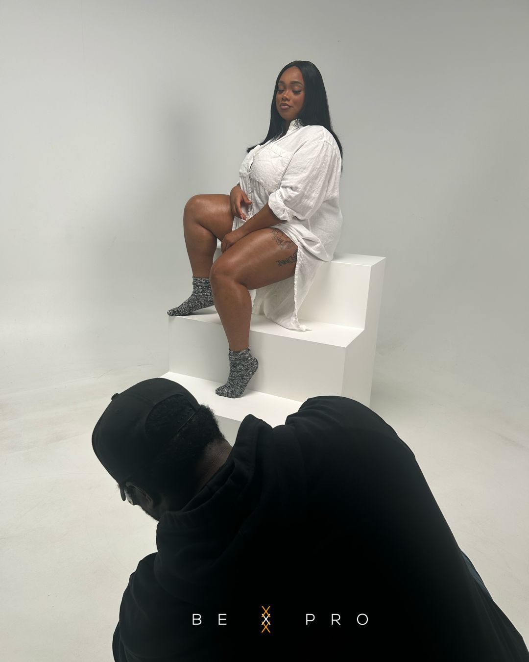A photographer captures a woman in a white shirt posing on white steps during a professional photo shoot.