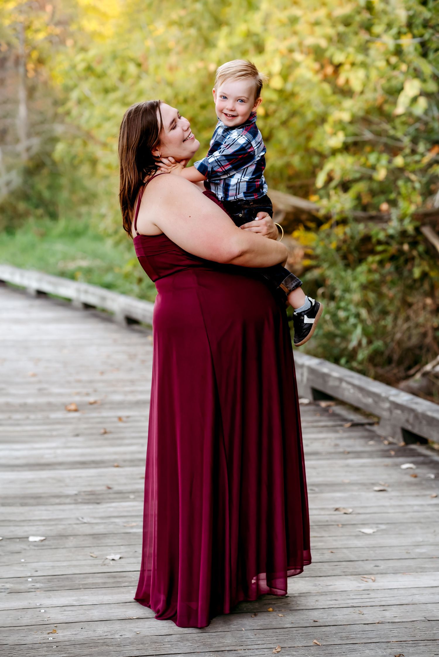 A tender moment captured on a wooden boardwalk with autumn foliage in the background.